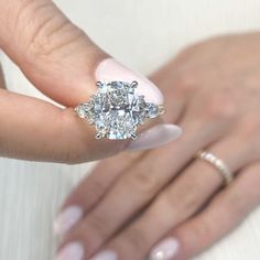 a woman's hand holding an engagement ring with three diamonds on it and two fingers