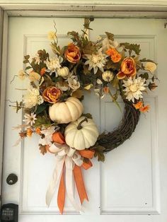 a wreath with flowers and pumpkins hanging on the front door