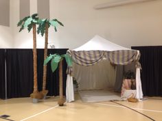 a tent set up with palm trees and drapes on the floor in front of it