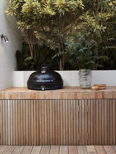 a grill sitting on top of a wooden table next to a bush filled with green leaves