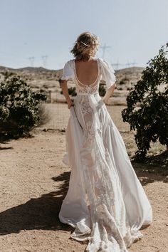 a woman standing in the desert wearing a white dress with sheer sleeves and an open back