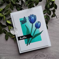 a card with blue tulips and a butterfly on it next to some green leaves