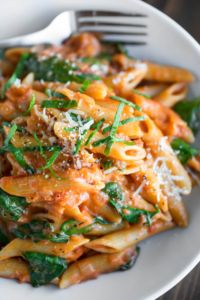 a white bowl filled with pasta and spinach covered in sauce on top of a wooden table