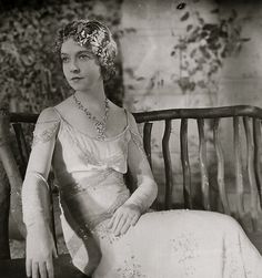 an old black and white photo of a woman sitting on a bench wearing a dress