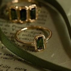 two rings sitting on top of an open book with green ribbon next to each other