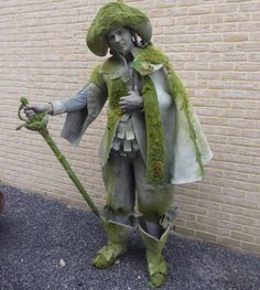 a statue of a man dressed in green and holding a stick with moss on it