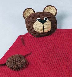 a crocheted teddy bear wrapped in a red blanket with brown ears and tail