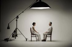 a man and woman sitting on chairs in front of a light