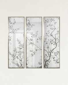 three glass panels hanging on the wall in front of a white wall with flowers and branches