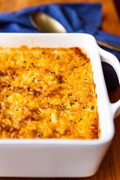 a casserole dish with cheese in it on a wooden table next to a spoon