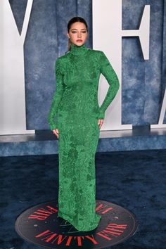 a woman in a green dress standing on a blue carpet with her hands on her hips