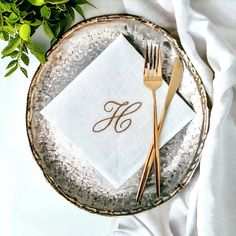 a silver plate topped with a napkin and two gold forks next to a green plant