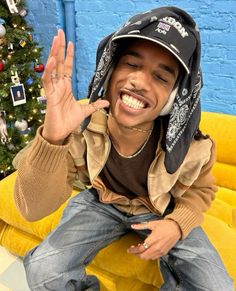 a man sitting on top of a yellow couch wearing a hat and making the peace sign