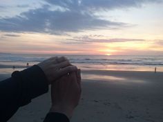 two hands holding each other on the beach at sunset with people in the water behind them