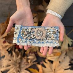 a woman's hand holding an old purse with buttons and beads on it, in front of leaves