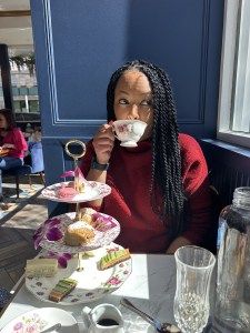 a woman sitting at a table drinking from a tea cup and saucer in front of her