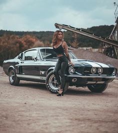 a beautiful woman standing next to a black mustang in front of a train track with a baseball bat on her shoulder