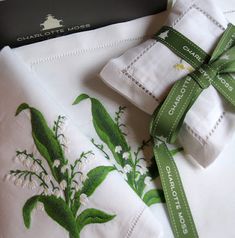 two napkins with green and white flowers on them next to a black business card