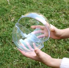 a person holding a clear plastic object in their hand on the grass with one hand reaching for it