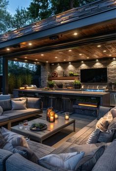 an outdoor living area with couches, tables and grill in the background at night