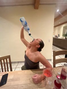 a woman sitting at a table drinking from a water bottle and holding a glass in her hand