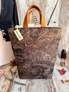 The Atenti Chester Hope Basket has faded black velvet with a rich printed design. Warm gold and brown tones mix elegance and earthy.  The Atenti Chester Hope Basket is a roomy stand-alone project bag. The top rolls down for easy access. The Atenti Hope Basket features a wide opening and two handles. Fully lined in light tan water-resistant taffeta. Inside are several pockets for tools and miscellaneous items. Atenti Hope Basket measures 12″ tall x 8″ wide x 8″ deep. (Miscellaneous items pictured Knitting Needle Storage, Handcrafted Handbags, Local Yarn Shop, Project Bags, Tool Pouch, Project Bag, Eyeglass Case, Accessory Pouch, Hand Dyed Yarn