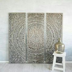 a vase sitting on top of a white stool next to a wall with an intricate design