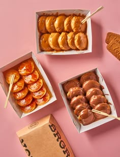 three boxes filled with donuts on top of a pink table next to a box of oranges