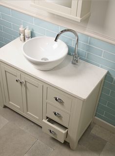 a bathroom sink sitting on top of a white counter next to a mirror and blue tiled walls