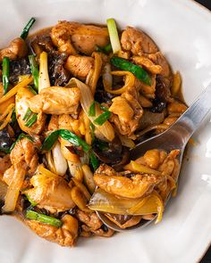 a white bowl filled with chicken and vegetables on top of a wooden table next to a fork