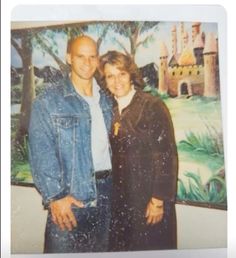 a man and woman standing next to each other in front of a painting on the wall