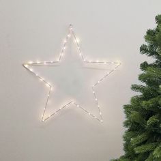 a lighted star hanging on the wall next to a small christmas tree with lights around it