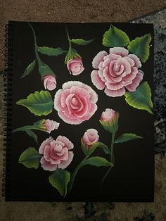 a black notebook with pink flowers painted on the cover and green leaves around it, sitting on a carpeted surface