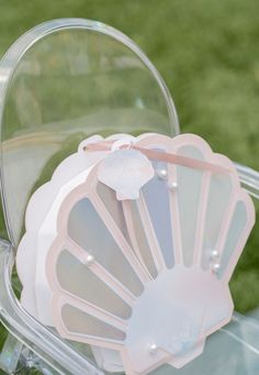 several fan shaped items are sitting in a clear case on the grass, and one has a pink ribbon attached to it