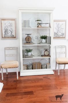 a white china cabinet sitting on top of a hard wood floor next to two chairs