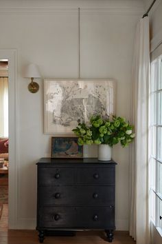 a black dresser with flowers on top in front of an open door and a painting hanging above it