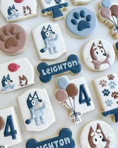 decorated cookies with dogs and balloons are displayed on a white tablecloth that is laid out to spell the number four