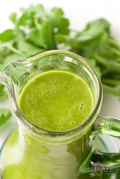 a pitcher filled with green liquid next to greens