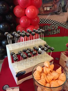 there are many desserts on the table with red and black balloons in the background