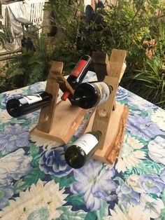 two wine bottles are placed in wooden racks on a tablecloth with flowers and vines