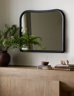 there is a mirror and some books on the shelf in front of this dresser with a plant