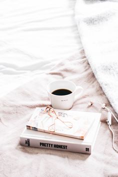 a cup of coffee sitting on top of a book next to a white bed sheet