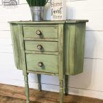 a green cabinet with three drawers and a potted plant on top of it, against a white wall