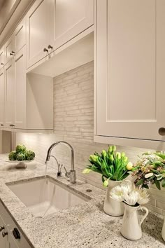 a kitchen with marble counter tops and white cabinets, along with green plants in vases