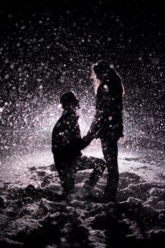 two people standing in the snow at night with one holding the other's hand