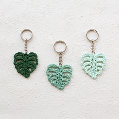 three key chains with green and blue crocheted leaves hanging from them on a white wall