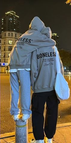 a man standing on the side walk with his back turned to the camera, wearing a jacket that says homeless