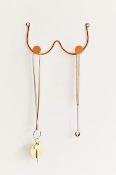 two gold and silver necklaces hanging from hooks on a white wall next to each other