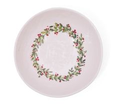 a white plate with holly and berries painted on the rim, against a white background