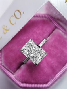 an engagement ring with a princess cut diamond set in a pink velvet case on display